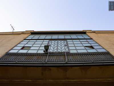 ...fino a quando alzando lo sguardo oltre le fronde ci appare alla vista un�antica ed elegante vetrata. Squadrata da un�intelaiatura in ferro reca al centro una sezione rettangolare impreziosita da elementi geometrici e in basso una fine ringhiera 